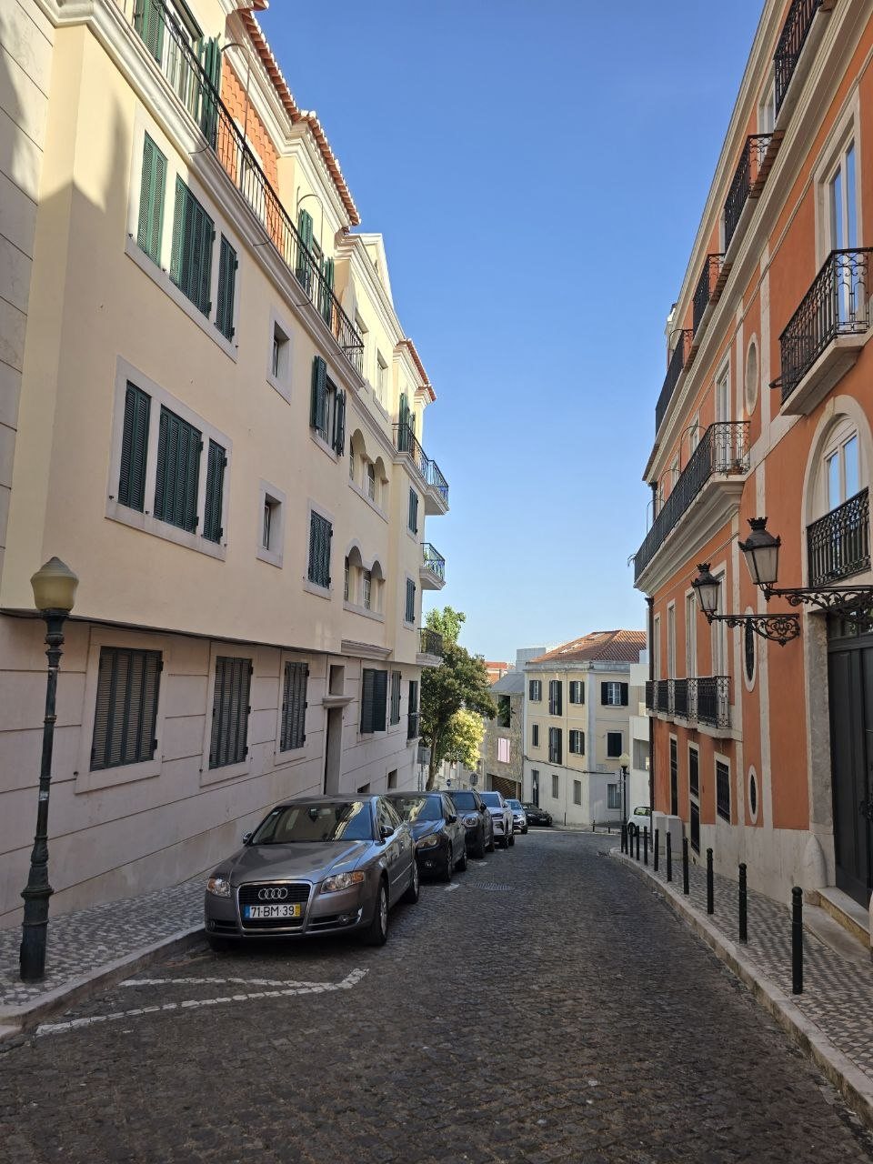 Sunny Lisbon street with colourful buildings, balconies, shutters, and parked cars